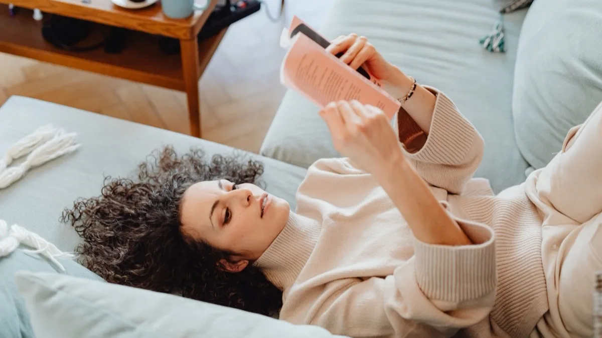Frau liegt entspannt auf dem Sofa und liest ein Buch