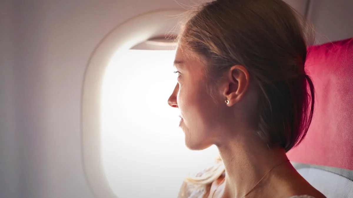 Frau schaut in einem Flugzeug ruhig aus dem Fenster ins Licht
