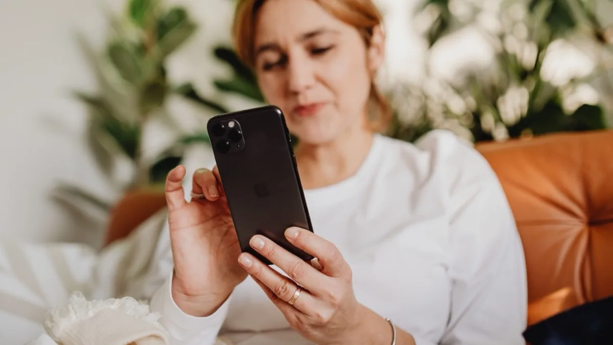 Frau sitzt auf dem Sofa und schaut nachdenklich auf ihr Smartphone
