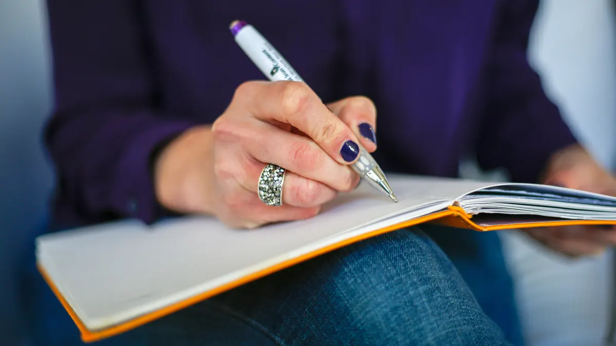 Frau schreibt konzentriert mit Stift in ein Notizbuch