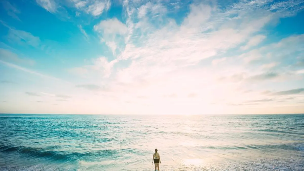 Frau steht allein am Strand und blickt aufs weite Meer